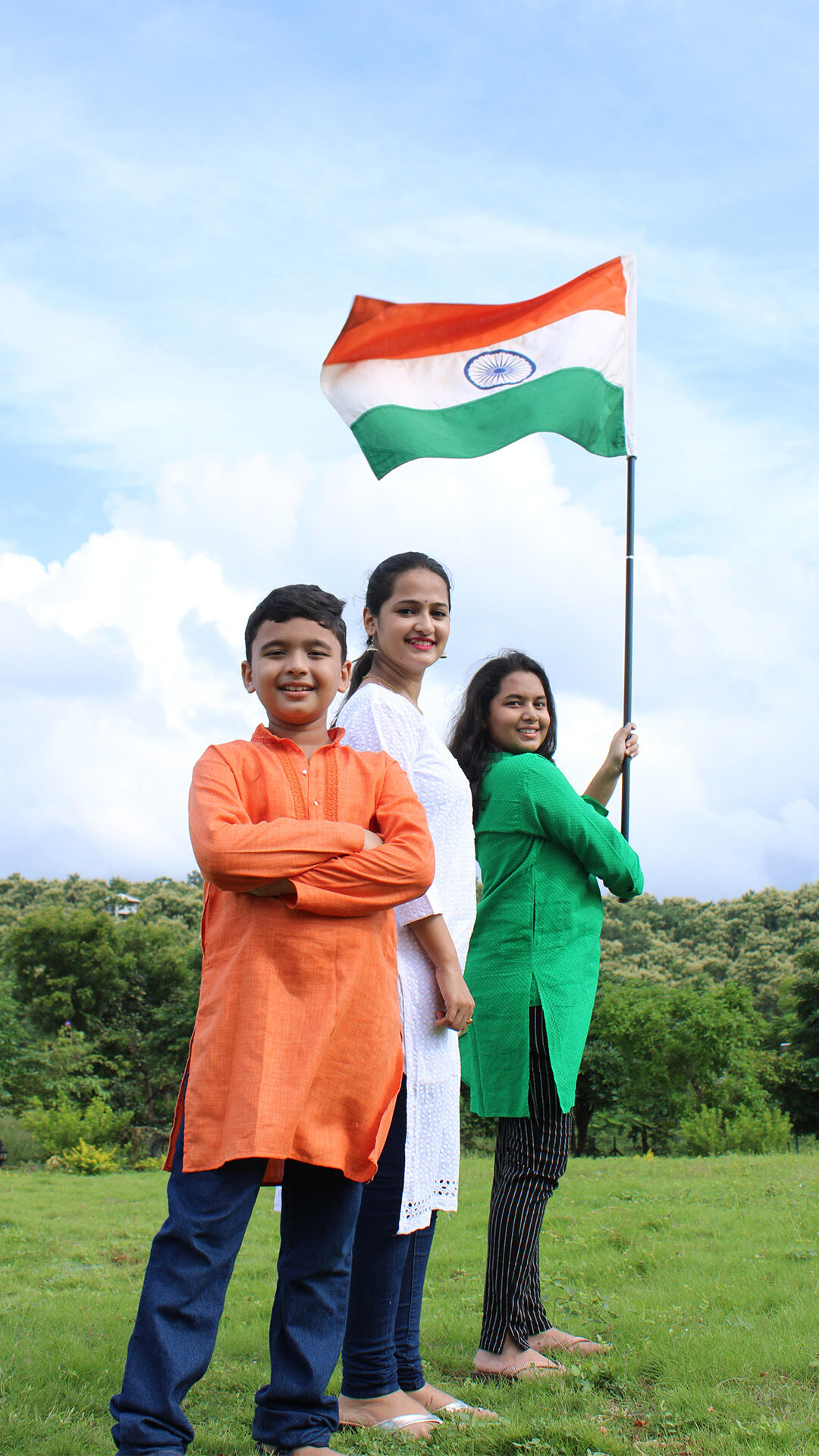 Happy Indian family in traditional attire celebrating Independence Day outdoors with the national flag.
